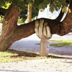 A carved wooden hand supporting a heavy tree branch in a park