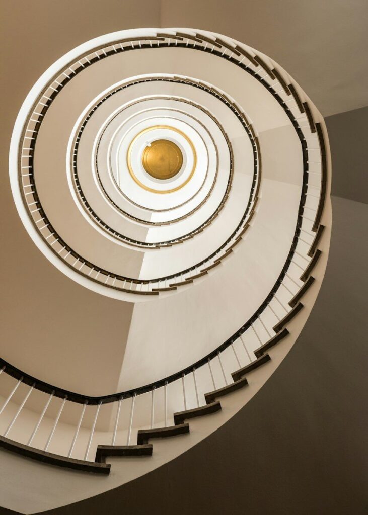 A spiral staircase viewed from below with a gold circular ceiling feature
